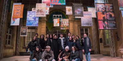 Studenti e visitatori nel cortile di Palazzo Zani durante l'inaugurazione serale della mostra, con i manifesti del progetto Bonifica Renana appesi sopra di loro